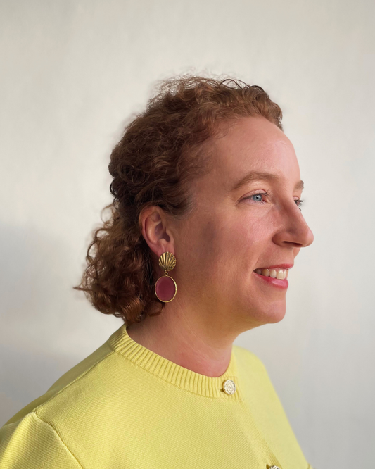 Lina lleva los pendientes Concha. Concha dorada con colgante de piedra rosa.