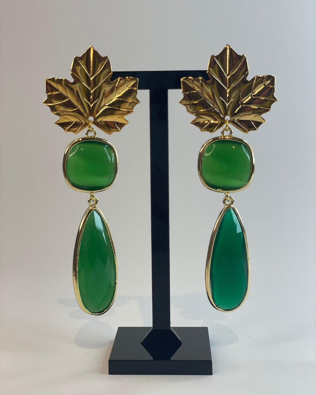 Vista frontal de los pendientes Brillo Otonal. El pendiente tiene un cierre de oro y dos piedras verde como colgante.