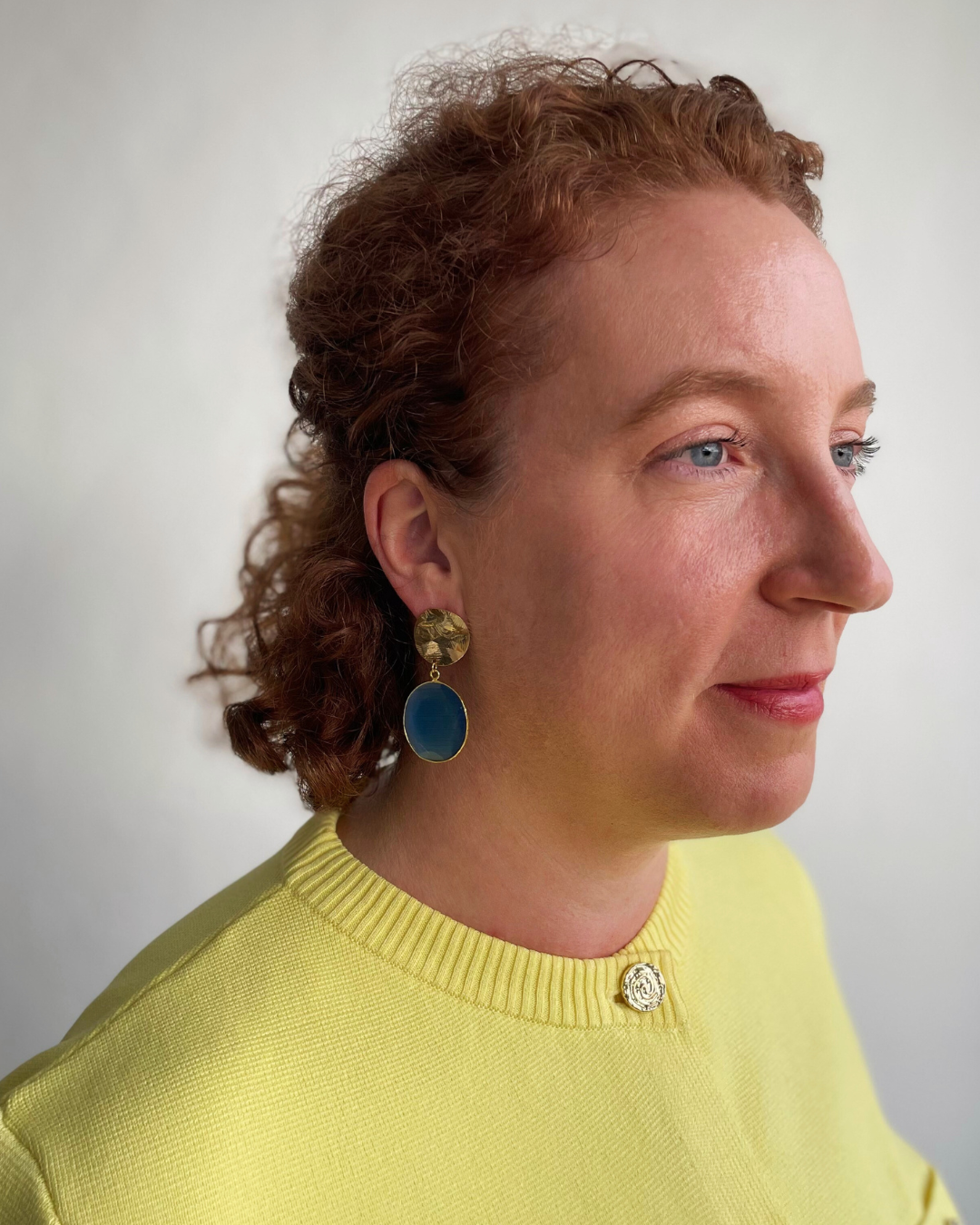 Lina lleva los pendientes Espejo de Cielo. Espejo de Cielo dorada con colgante de piedra azul.