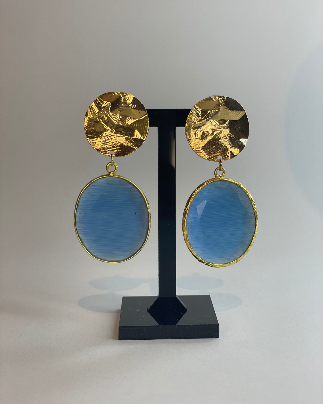 Vista frontal de los pendientes Espeko de Cielo. El pendiente tiene un cierre de oro y una piedra azul como colgante.