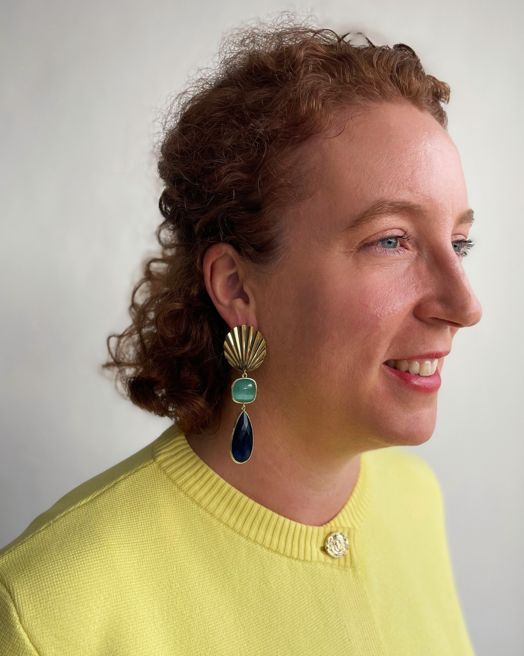 Lina lleva los pendientes Tesoro Marino. Tesoro Marino dorada con colgante de piedra aqua verde y azul.